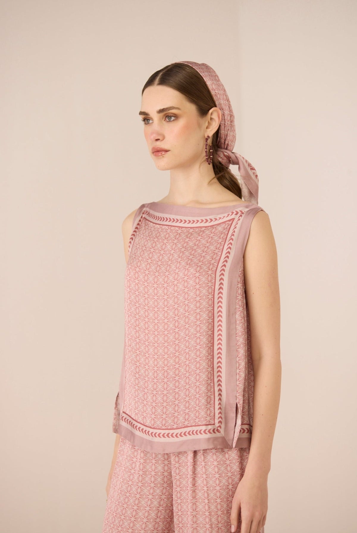 Woman wearing a pink patterned top and headscarf against a beige background Calling June