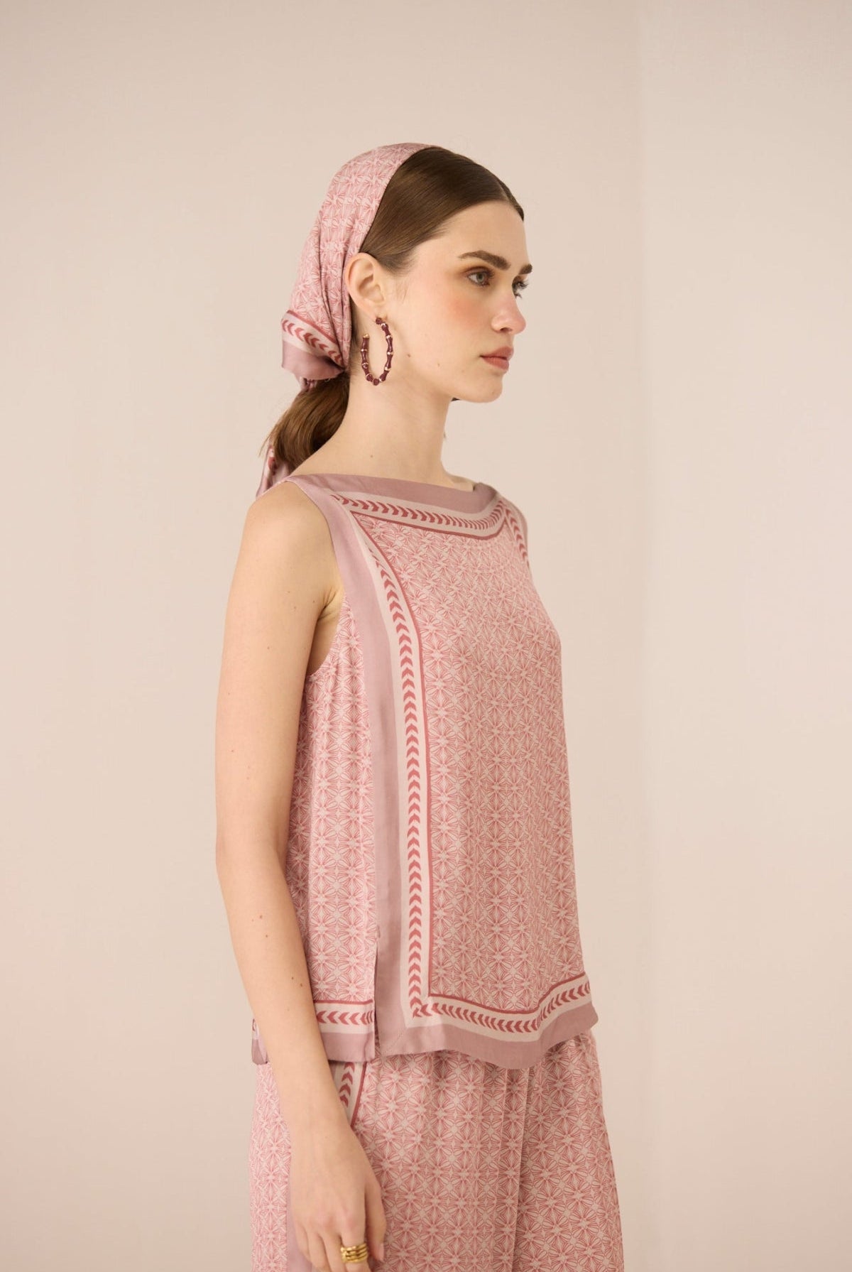 Woman wearing a pink patterned top and headscarf against a beige background Calling June