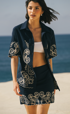 Woman wearing a black embroidered jacket and skirt on a beach Calling June