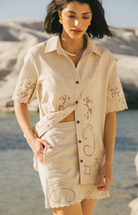 Woman wearing a beige embroidered outfit by a body of water Calling June
