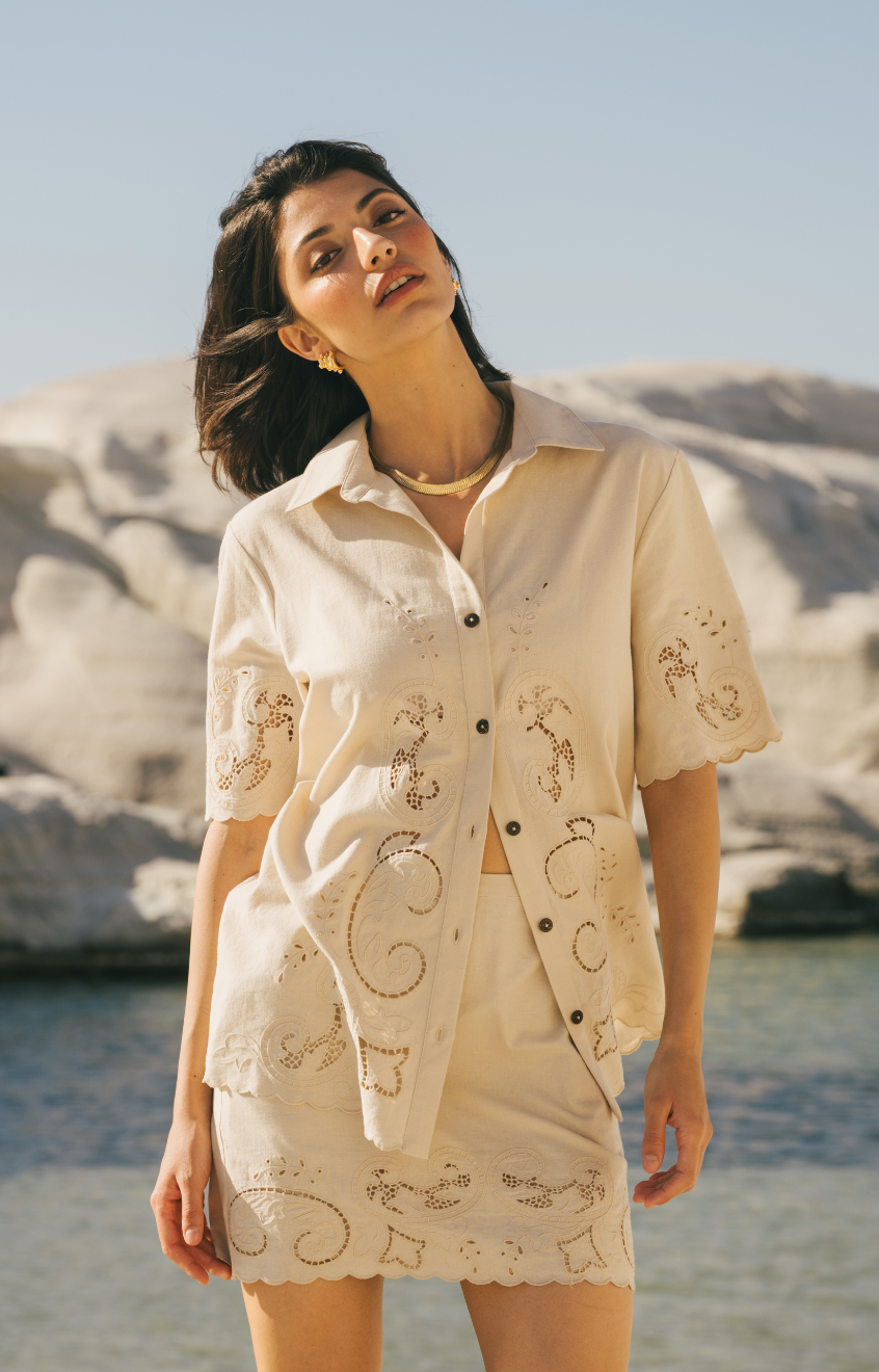 Woman wearing a beige embroidered outfit on a beach with sand dunes in the background Calling June