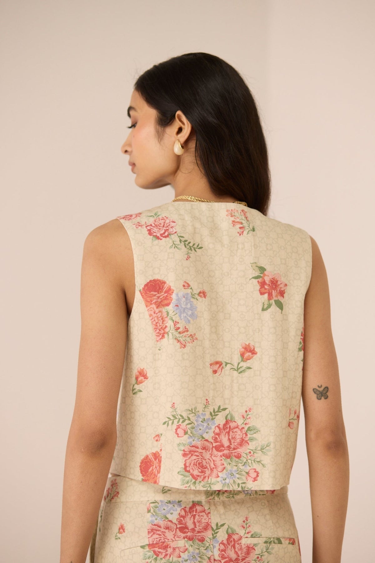 Woman wearing a floral embroidered sleeveless top against a beige background Calling June