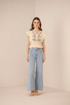 Woman wearing a beige embroidered top and light blue jeans on a beige background Calling June