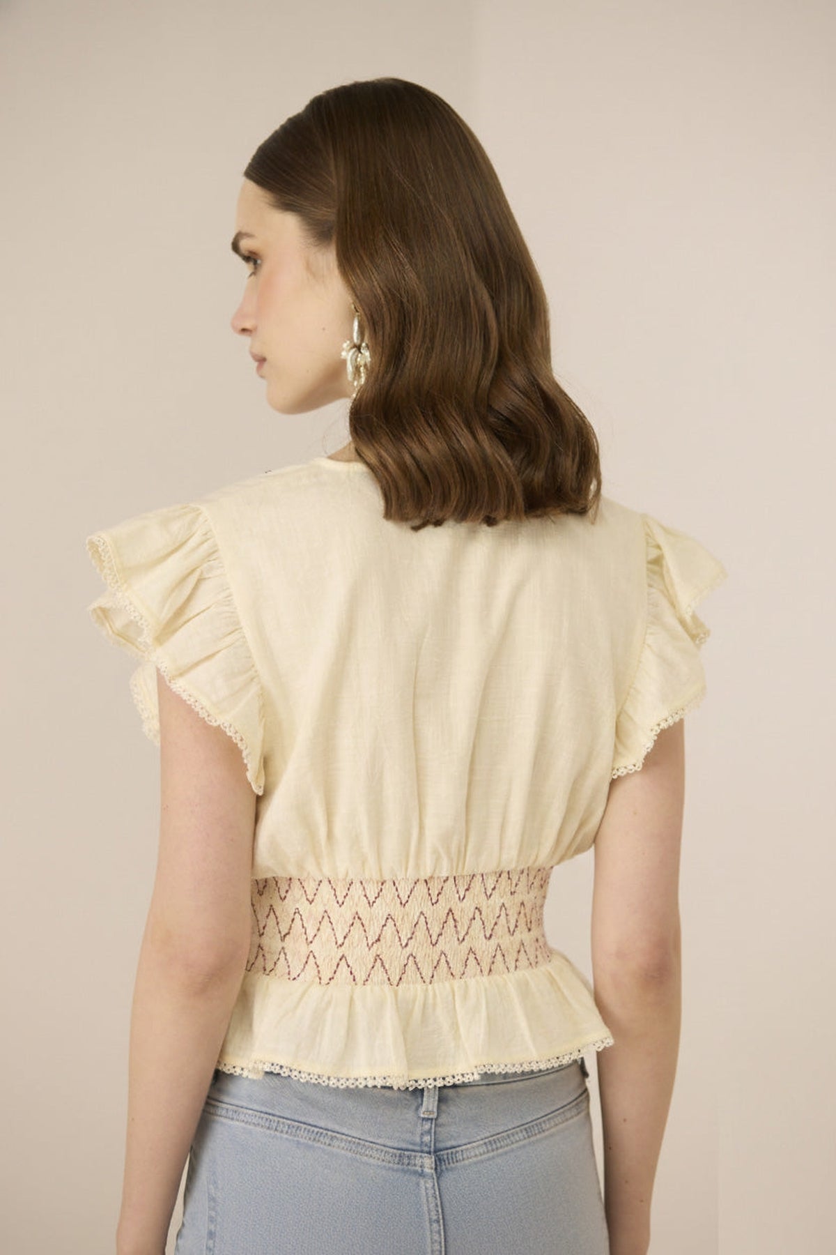 Woman wearing a light-colored blouse with ruffled sleeves and a subtle pattern on a plain background Calling June