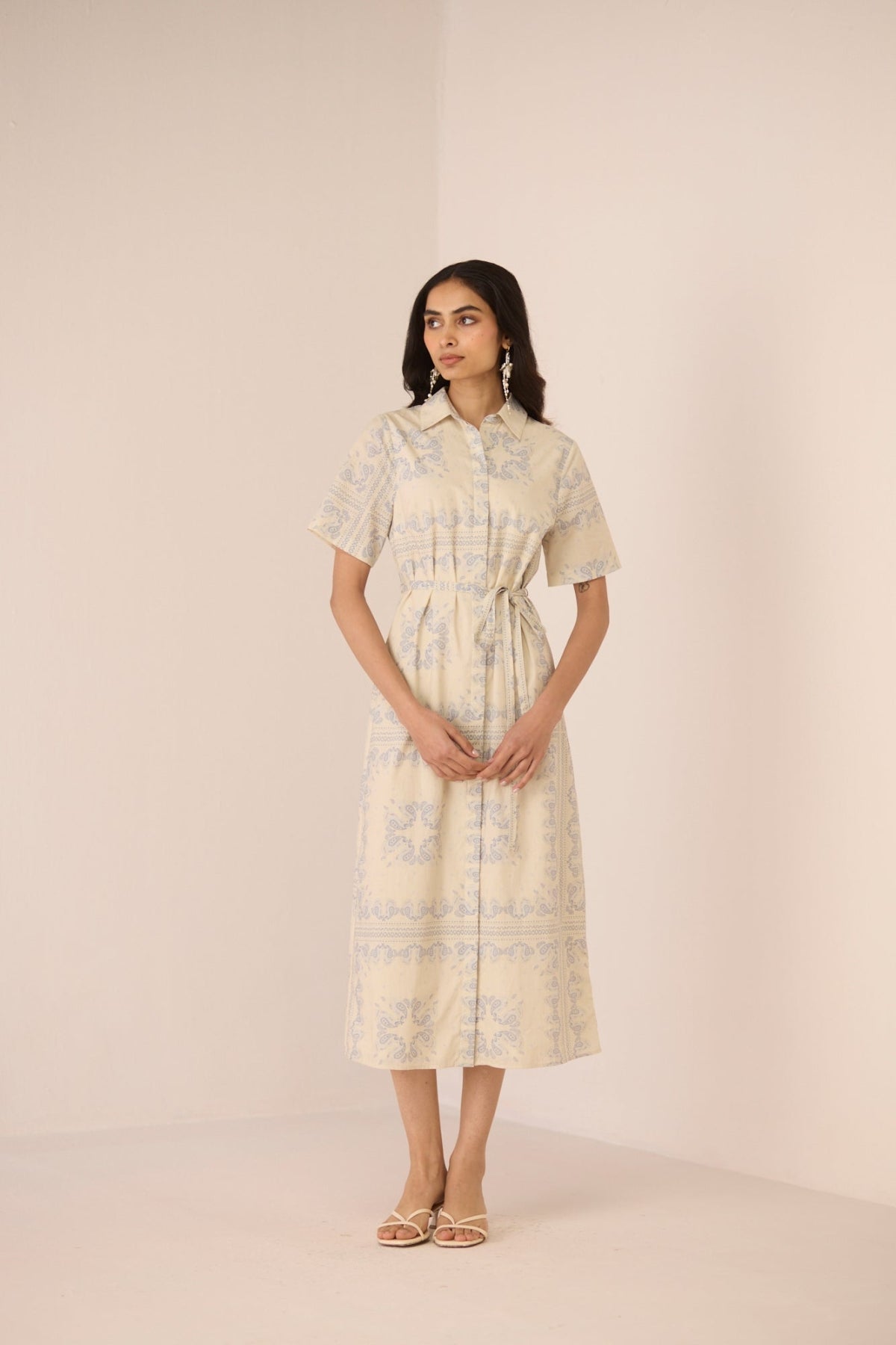 Woman wearing a light-colored dress with a subtle pattern on a plain background Calling June