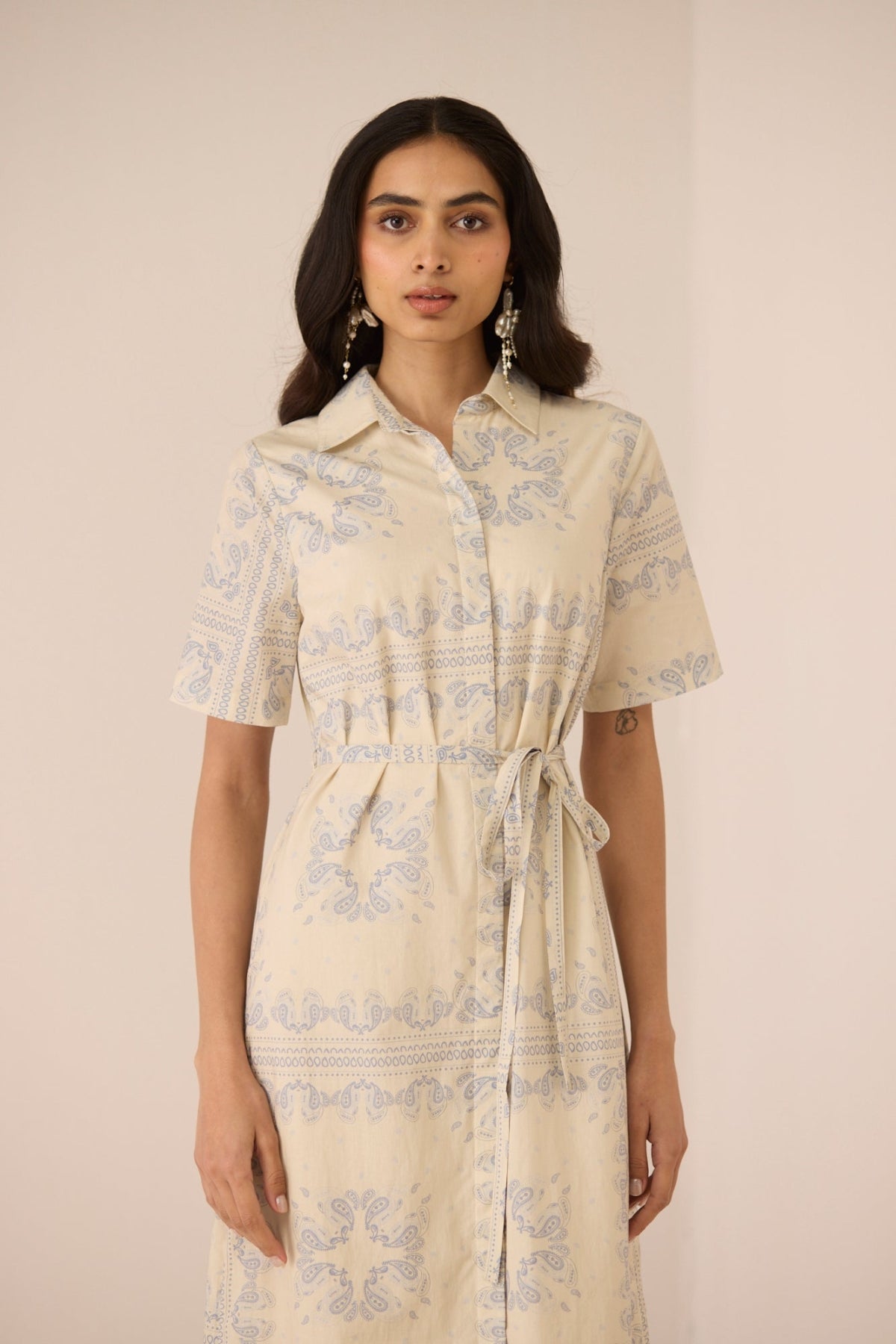 Woman wearing a beige dress with floral patterns against a plain background Calling June
