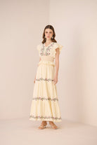 Woman wearing a light yellow set with floral embroidery on a beige background Calling June