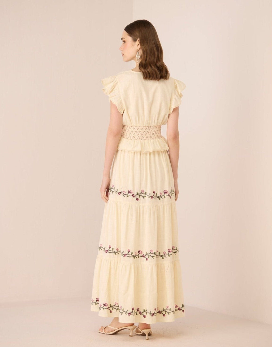 Woman wearing a light yellow set with floral embroidery on a beige background Calling June