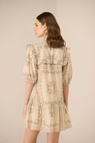 Woman wearing a beige floral dress against a plain background Calling June