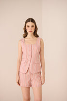 Woman wearing a pink striped outfit with a vest and shorts on a beige background Calling June