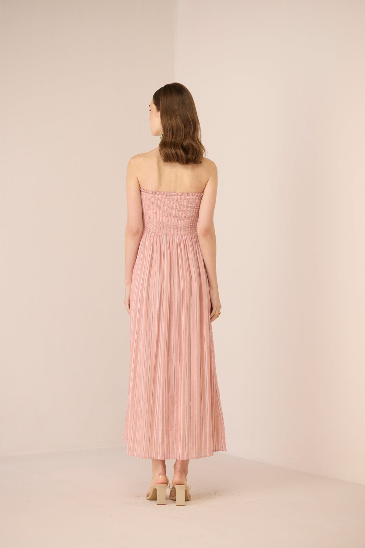 Woman wearing a pink strapless dress against a plain background Calling June