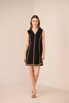 Woman wearing a black dress with gold trim on a beige background Calling June