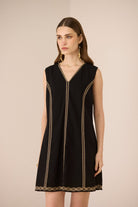 Woman wearing a black sleeveless dress with gold trim on a beige background Calling June