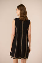 Black sleeveless dress with gold trim on a beige background Calling June