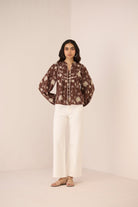 Woman wearing a patterned blouse and white pants against a plain background Calling June