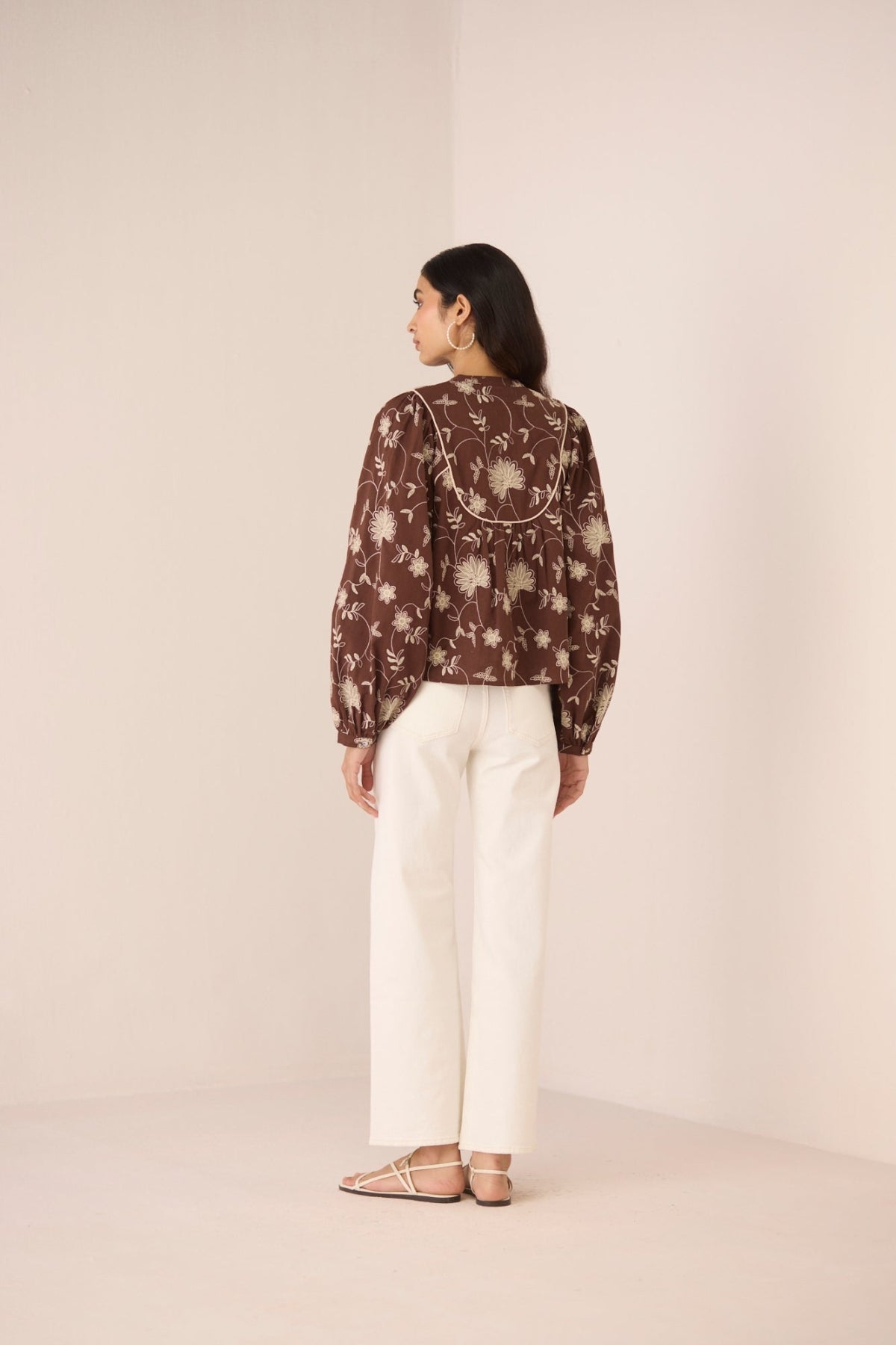 Woman wearing a brown floral blouse and white pants against a beige background Calling June