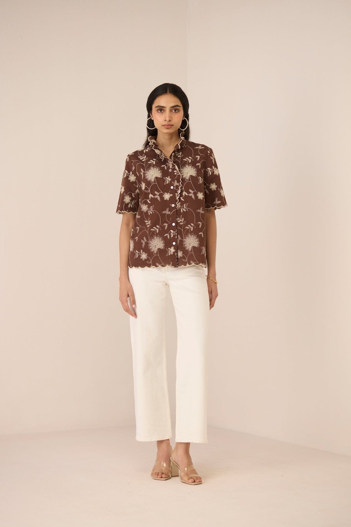 Woman wearing a brown floral blouse and white pants on a beige background Calling June