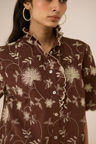Woman wearing a brown floral patterned shirt against a neutral background Calling June