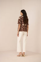 Woman wearing a brown floral blouse and white pants on a beige background Calling June