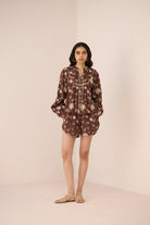 Woman wearing a brown floral dress against a plain background Calling June