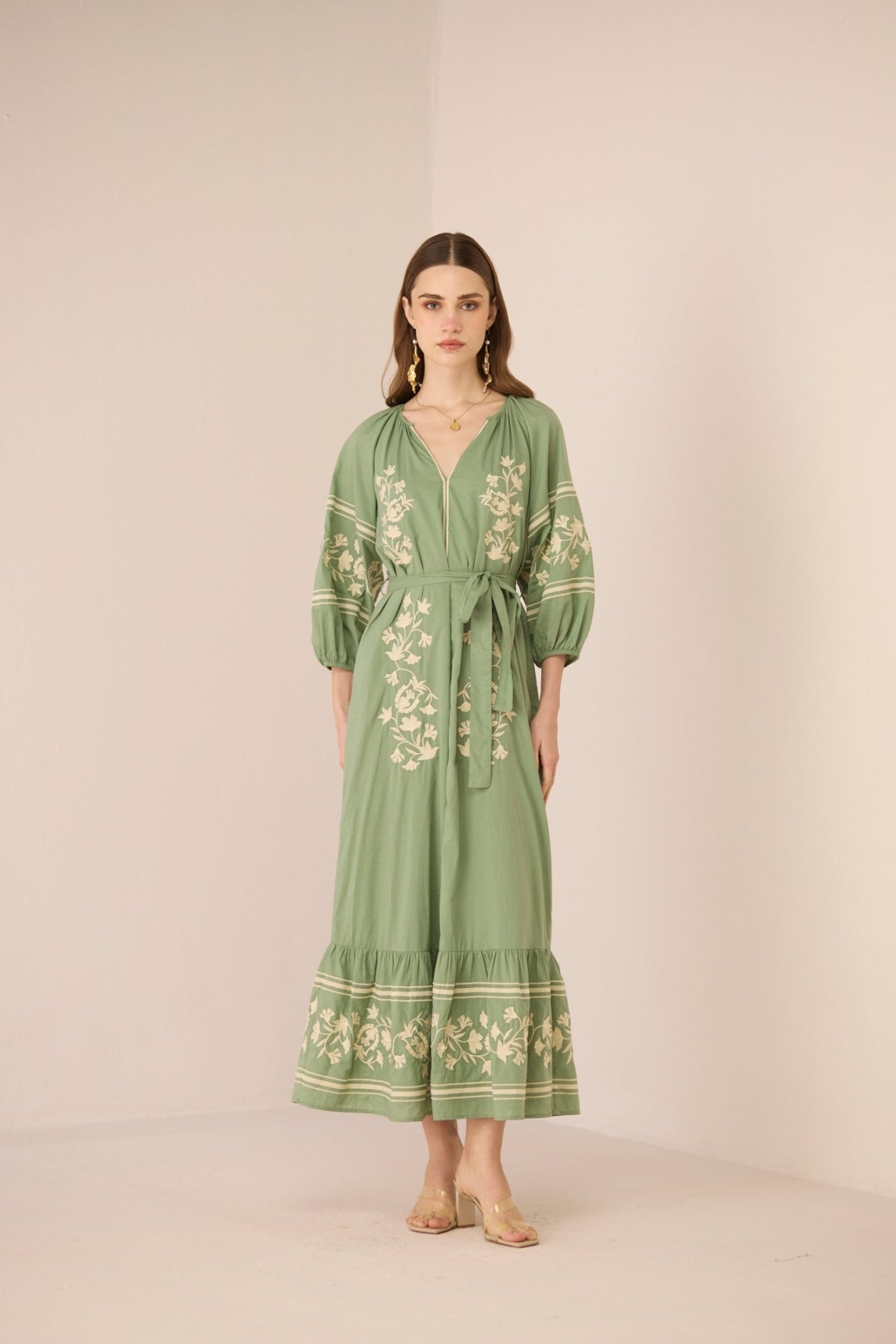 Woman wearing a green embroidered dress against a beige background Calling June