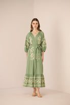 Woman wearing a green embroidered dress against a beige background Calling June