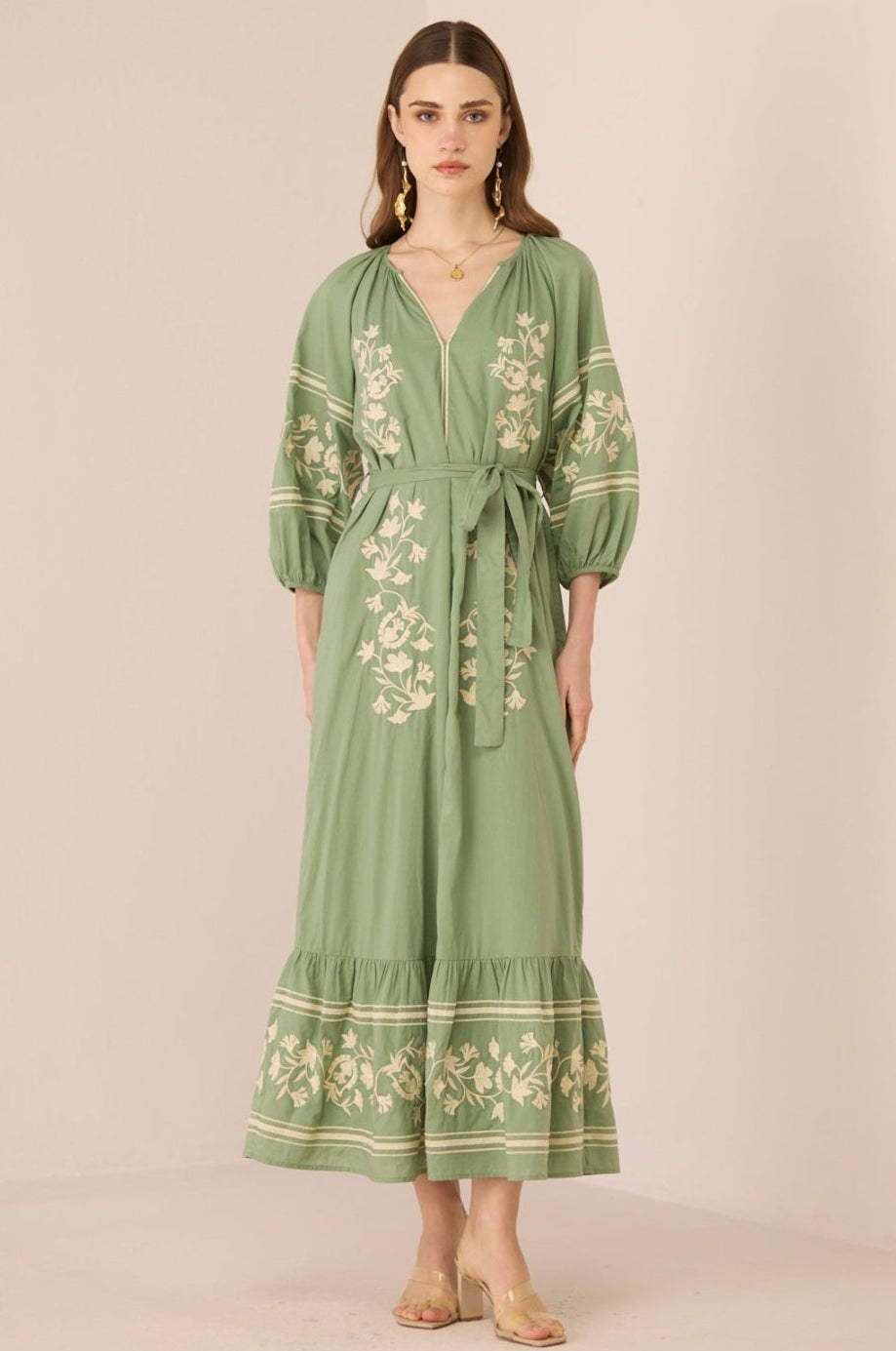 Woman wearing a green embroidered dress against a beige background Calling June