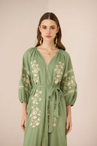 Woman wearing a green embroidered dress against a beige background Calling June