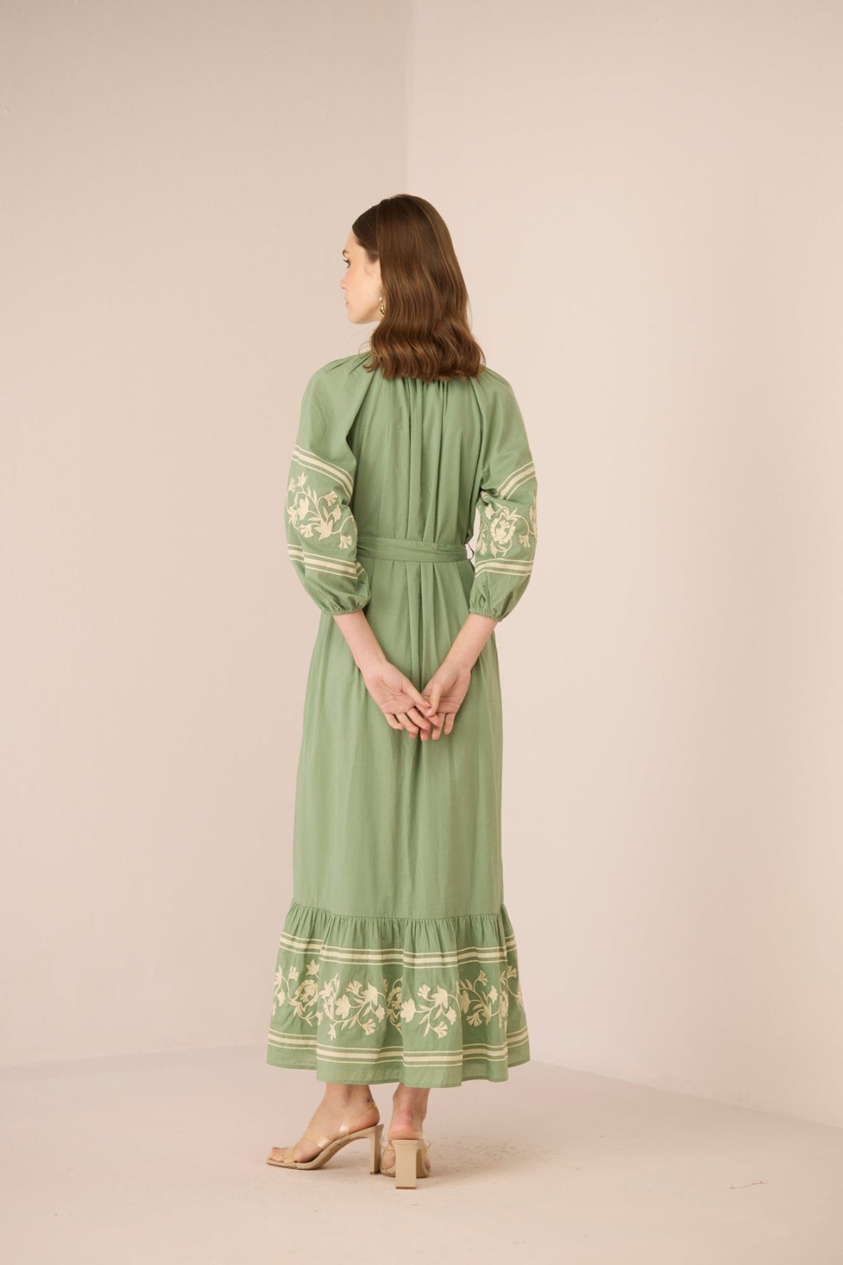 Woman wearing a green dress with floral embroidery on a beige background Calling June