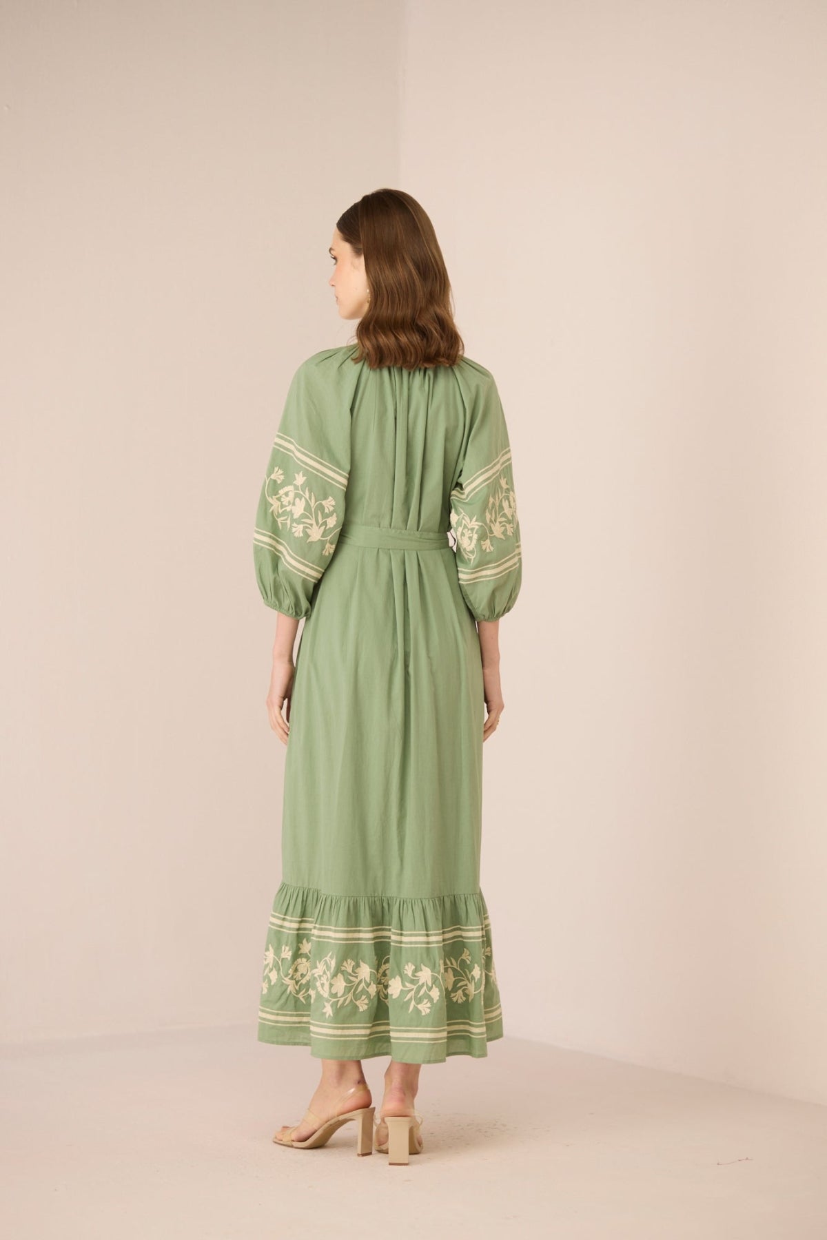 Woman wearing a green dress with floral embroidery on a beige background Calling June