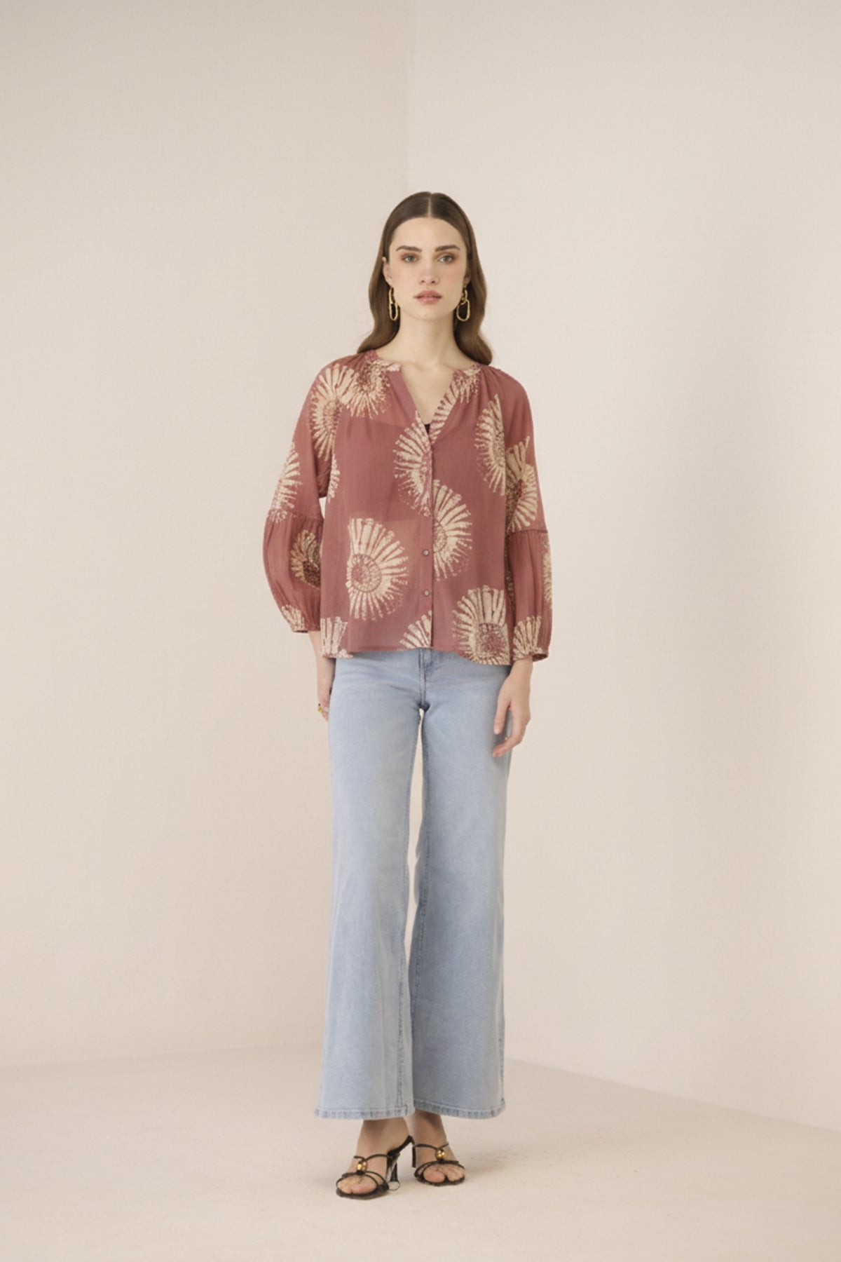 Woman wearing a patterned blouse and light blue pants on a beige background Calling June