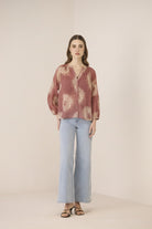 Woman wearing a patterned blouse and light blue pants on a beige background Calling June