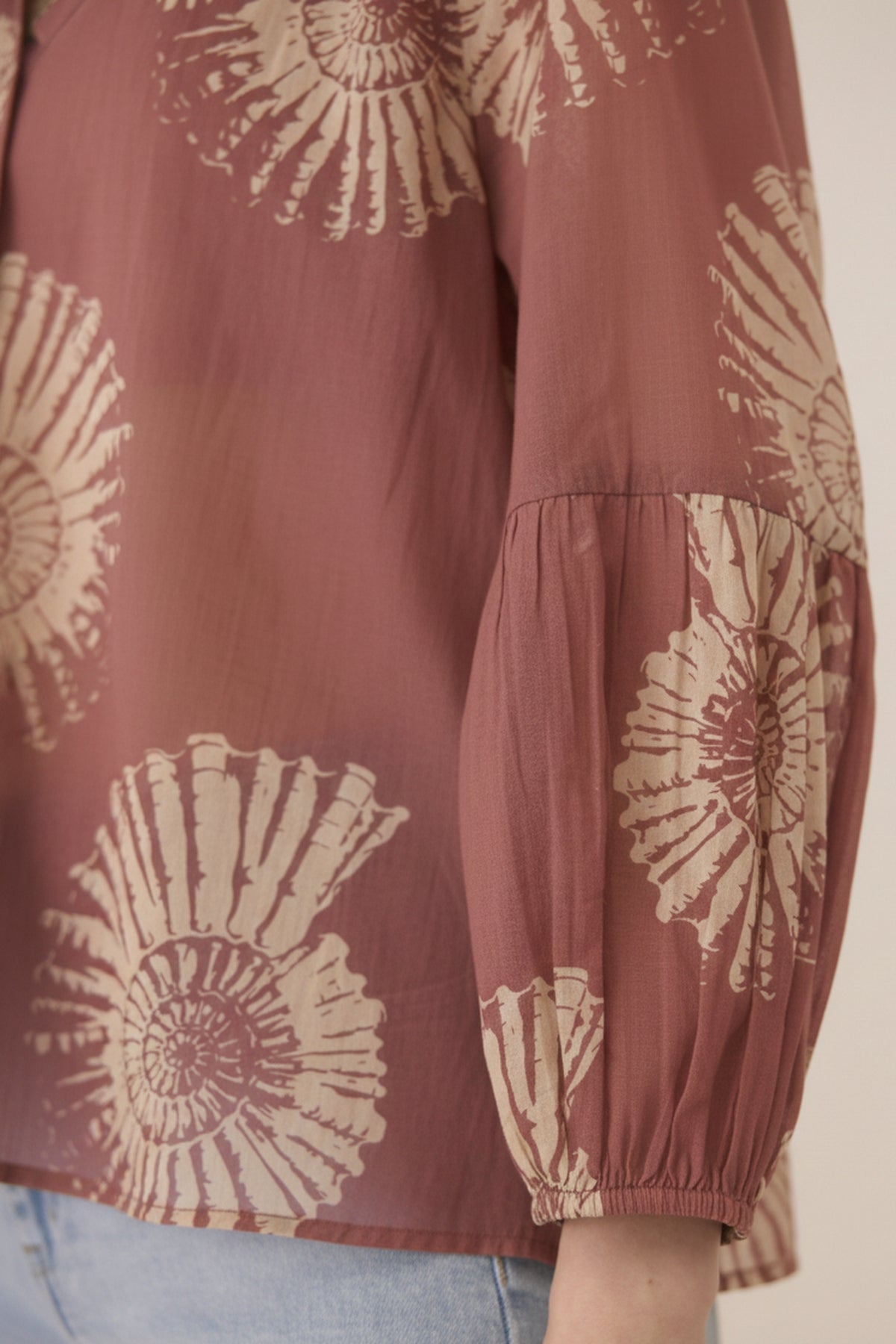 Brown blouse with beige floral patterns worn by a person, on a neutral background Calling June