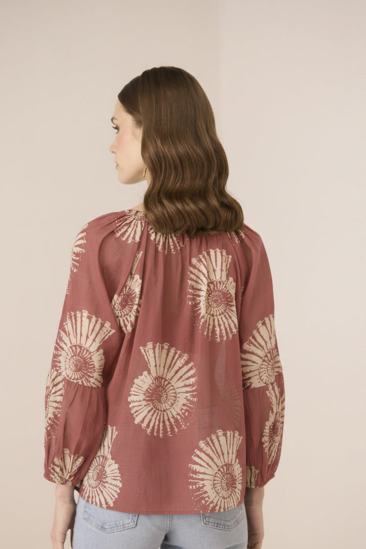 Woman wearing a rust-colored blouse with beige floral patterns on a plain background Calling June
