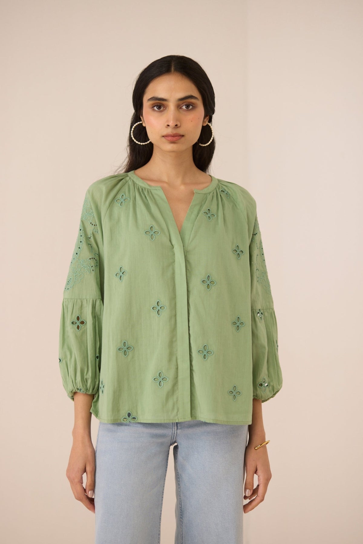 Woman wearing a green embroidered blouse against a beige background Calling June