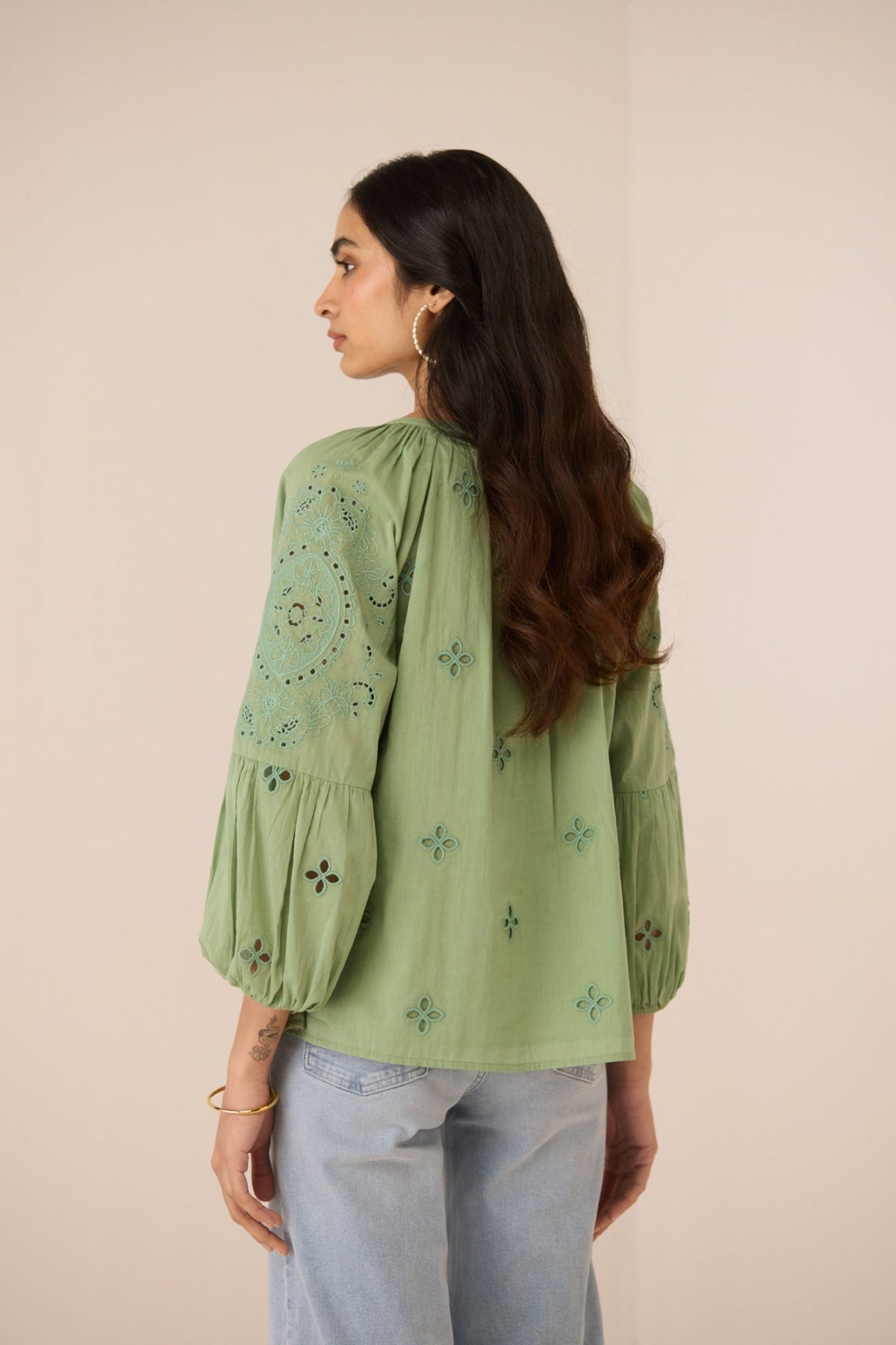 Woman wearing a green embroidered top with light blue jeans on a beige background Calling June