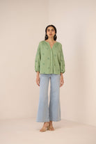 Woman wearing a green embroidered blouse and light blue jeans on a beige background Calling June