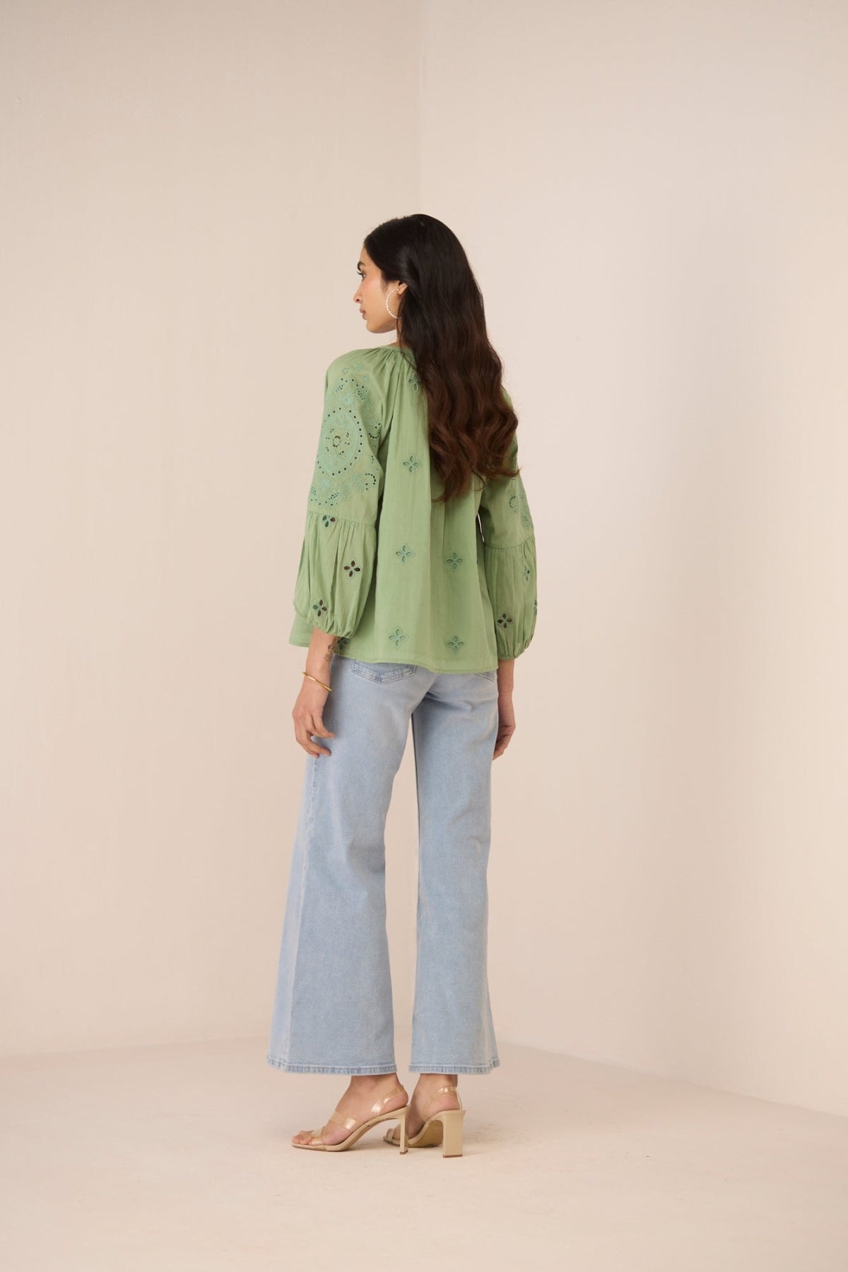 Woman wearing a green embroidered top and light blue jeans on a beige background Calling June
