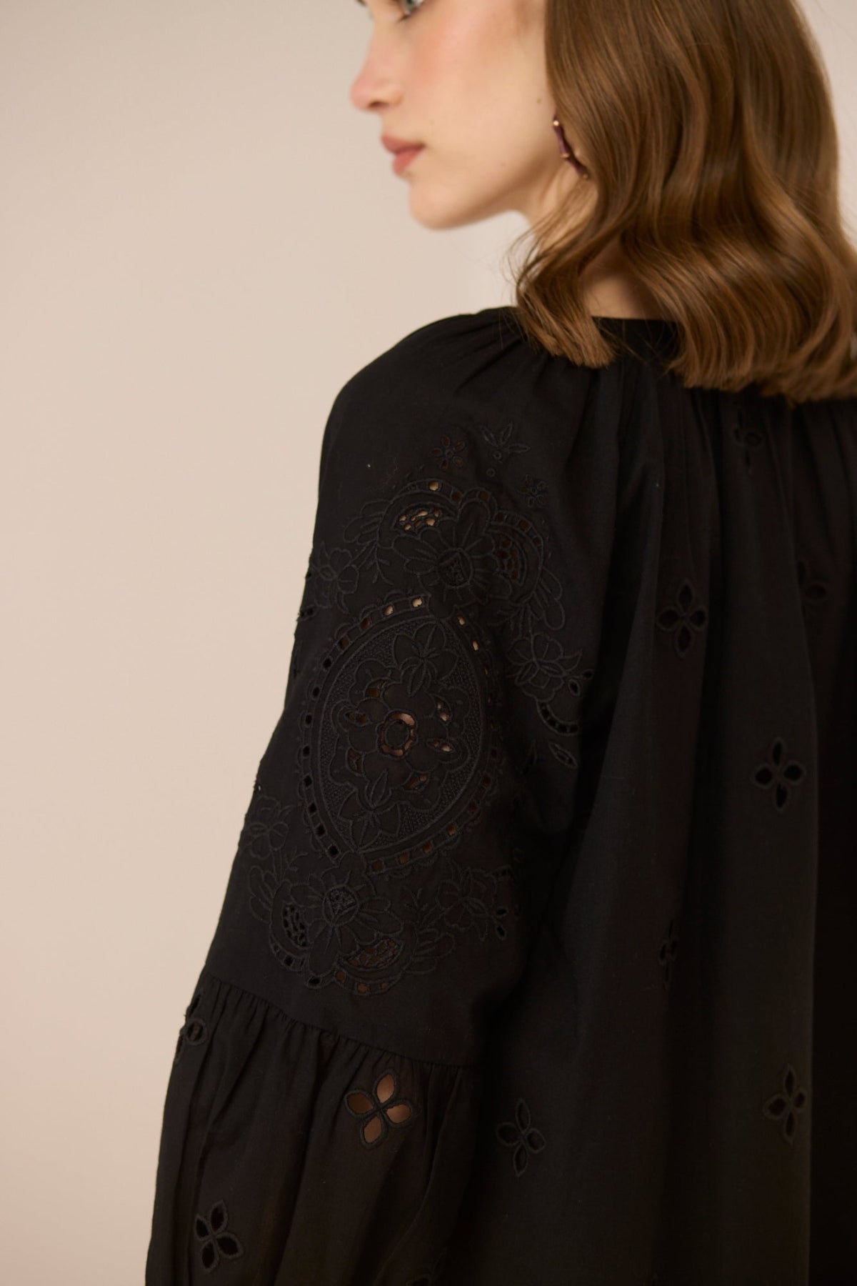 Black dress with intricate cut-out patterns on a beige background Calling June