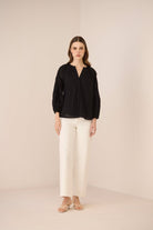 Woman wearing a black blouse and white pants on a beige background Calling June