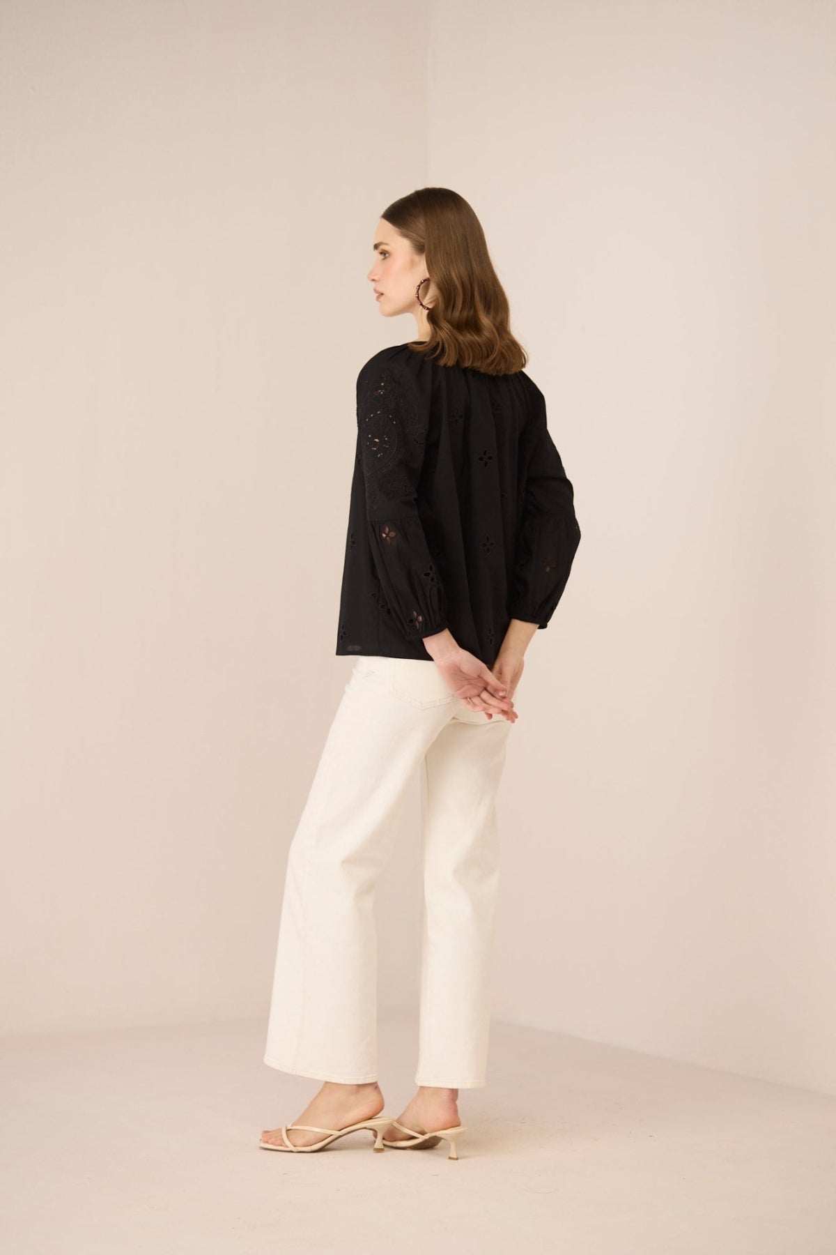 Woman wearing a black jacket and white pants against a beige background Calling June