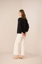 Woman wearing a black jacket and white pants against a beige background Calling June