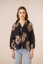 Woman wearing a black blouse with gold floral patterns on a beige background Calling June