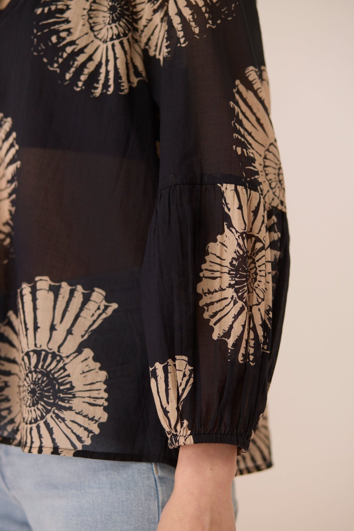 Black blouse with beige floral patterns worn by a person, on a neutral background Calling June