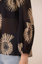 Black blouse with beige floral patterns worn by a person, on a neutral background Calling June