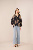 Woman wearing a black patterned blouse and light blue jeans on a beige background Calling June