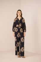 Woman wearing a black floral patterned outfit on a beige background Calling June