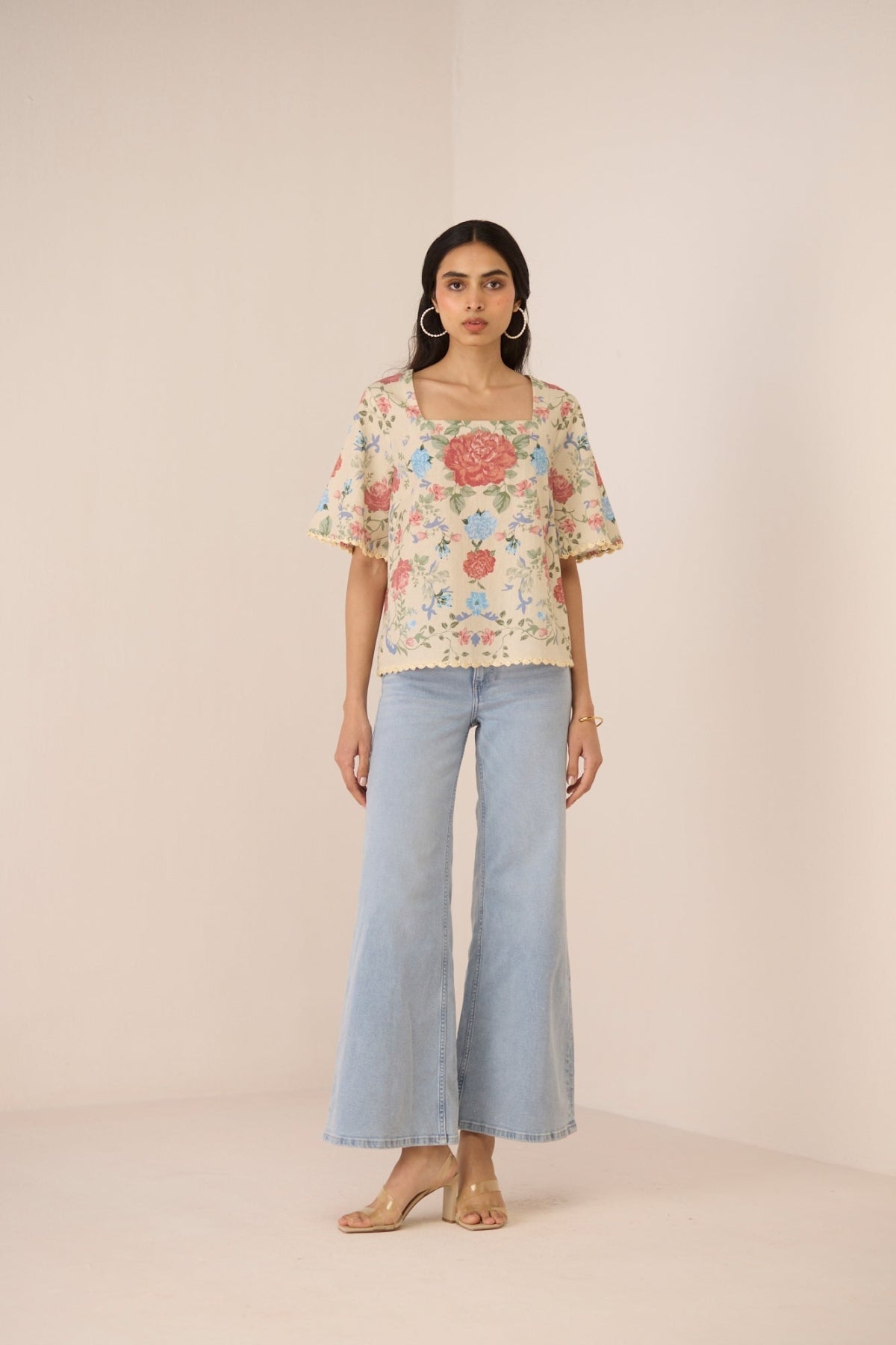 Woman wearing a floral blouse and light blue jeans on a beige background Calling June