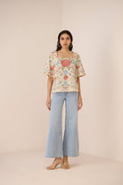 Woman wearing a floral blouse and light blue jeans on a beige background Calling June