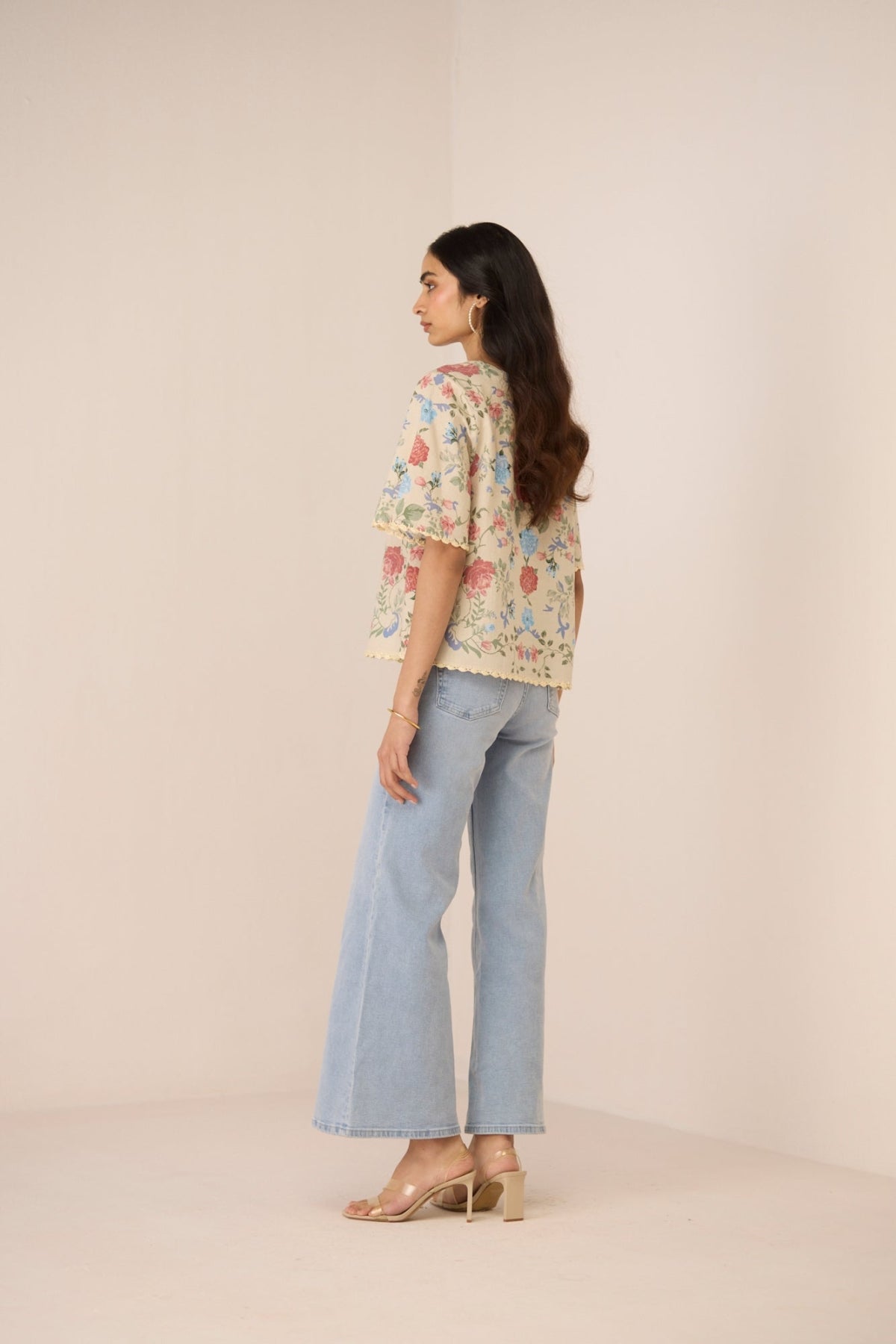 Woman wearing a floral blouse and light blue jeans on a beige background Calling June